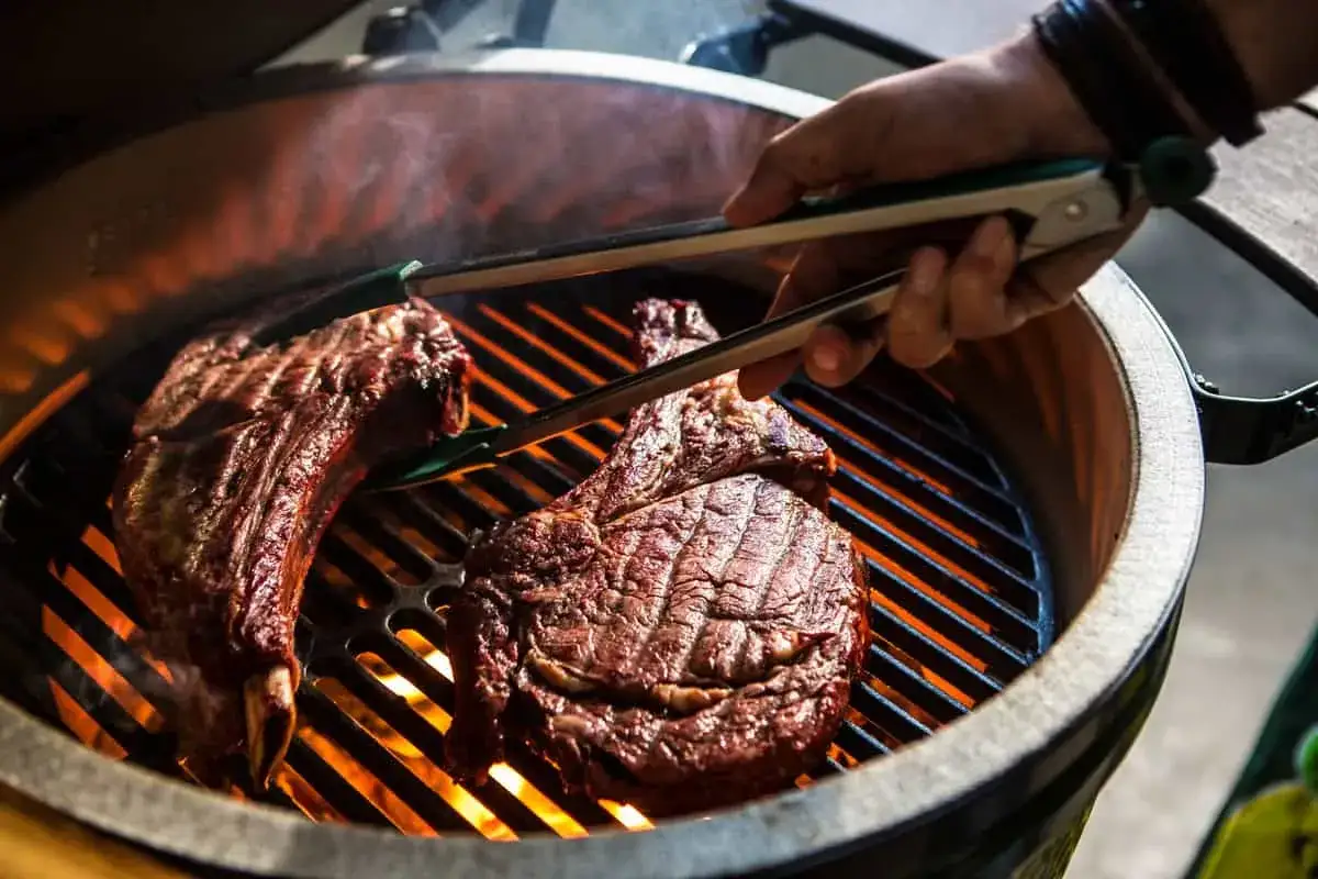 Deux belles côtes de bœuf sur un barbecue à gaz, prêtes pour le temps de cuisson idéal. La viande grésille sur les braises ardentes.