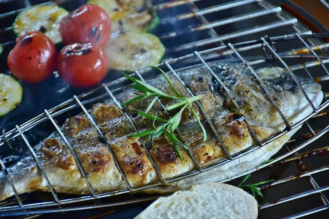 Poisson entier grill&eacute; sur un brasero, accompagn&eacute; de tomates et courgettes. Une branche de romarin parfume ce plat savoureux.