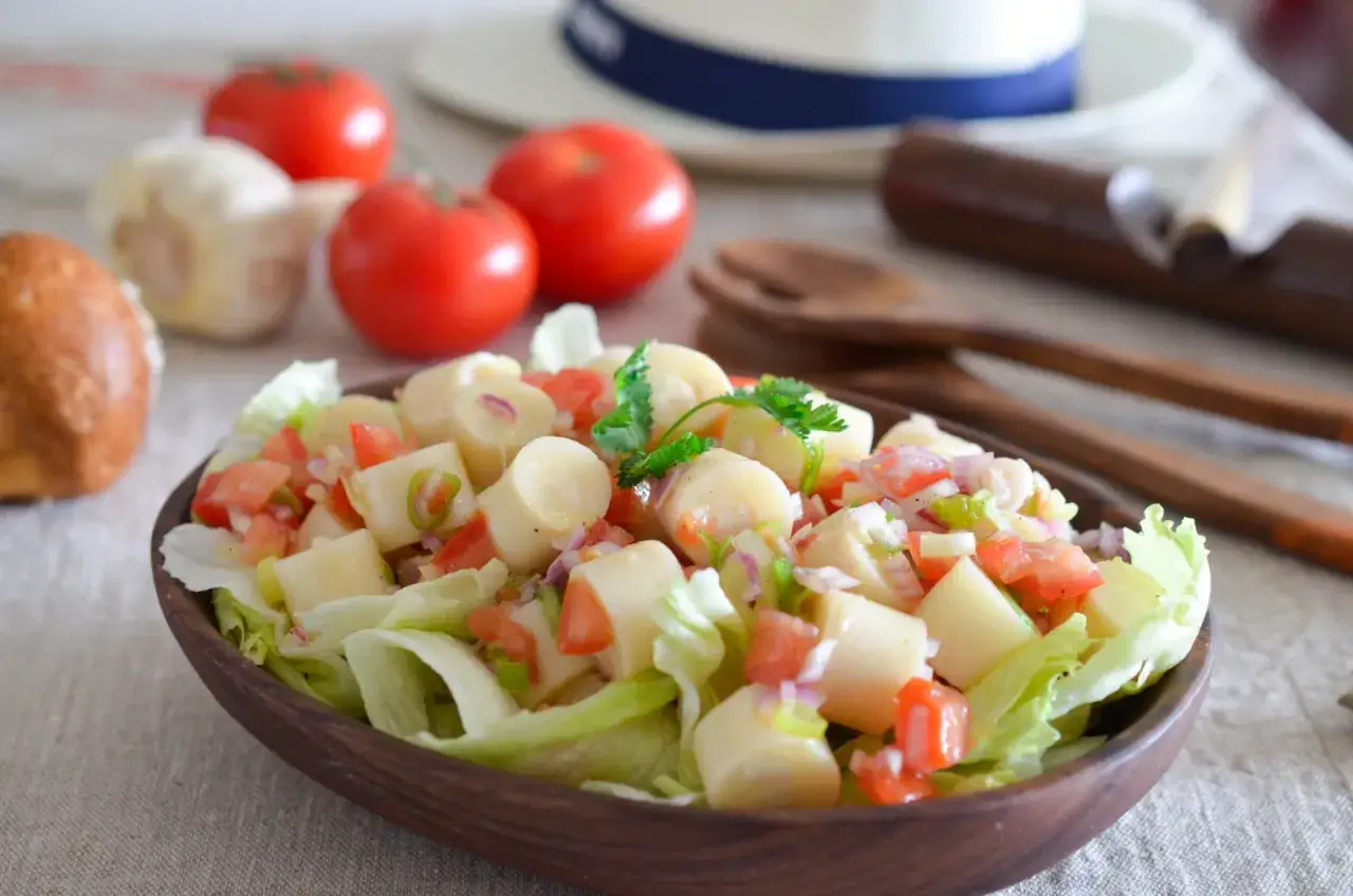 Salade fraîche et colorée de cœur de palmier, tomates, oignons rouges et persil, servie sur un lit de laitue dans un bol en bois.