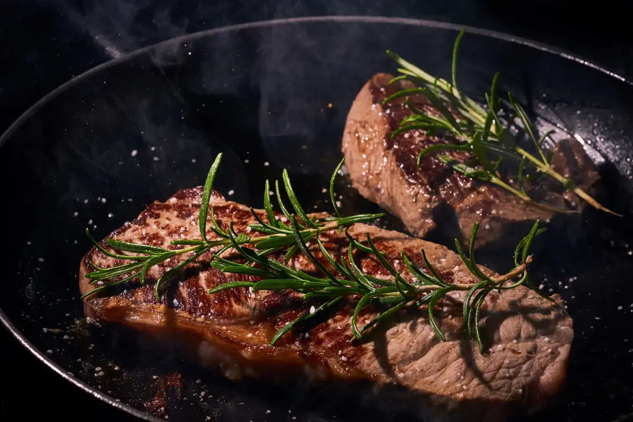 Deux steaks de boeuf Black Angus savoureux mijotent dans une poêle, ornés de romarin frais et de gros sel.