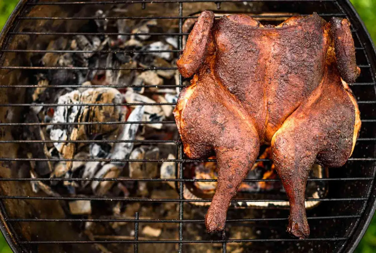 Un poulet fumé, doré et croustillant, cuit sur un barbecue avec des braises ardentes en dessous.