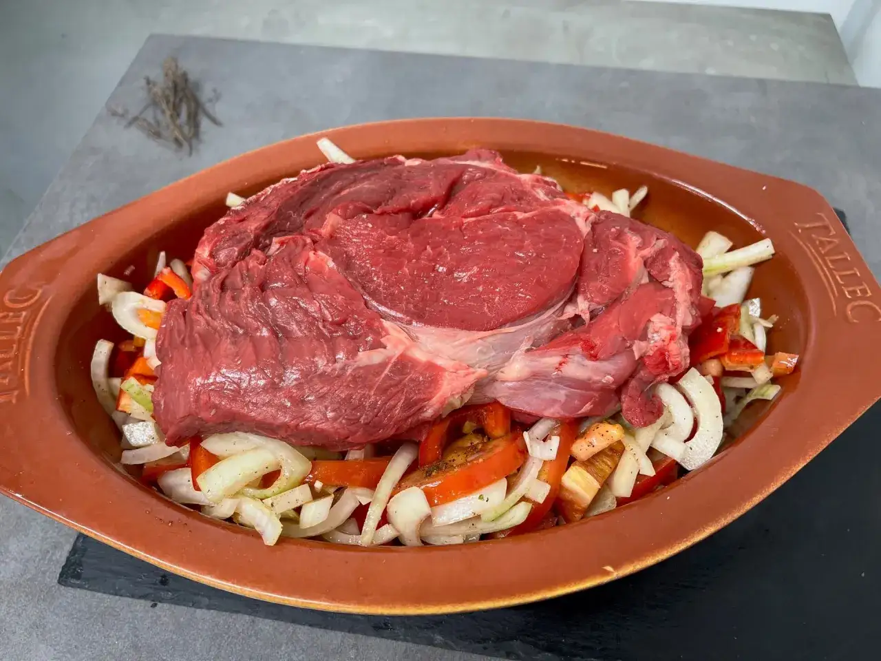 Une belle basse côte de bœuf crue, prête à être cuite avec des oignons et des poivrons dans un plat en terre cuite.