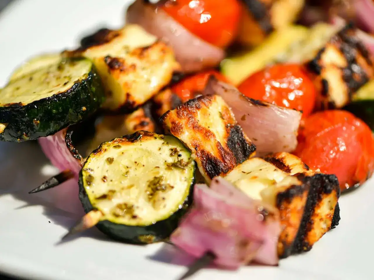 Brochettes de halloumi grillé avec courgettes, tomates cerises et oignons rouges. Parfaites pour un repas d'été au barbecue.