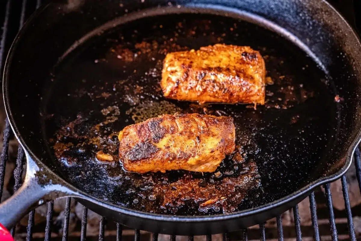 Deux morceaux de lieu noir, assaisonnés et poêlés dans une fonte sur un barbecue.