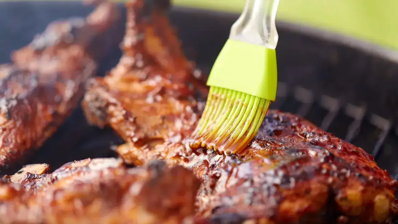 Un pinceau vert applique une sauce sur des côtes de porc grillées, une méthode pour comment donner un goût fumé aux aliments.