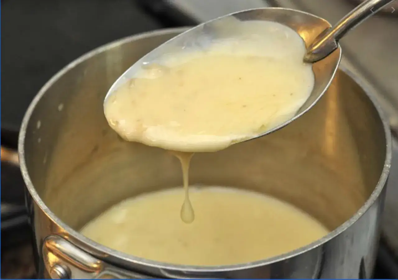 Une cuillère de sauce onctueuse, prête pour une recette beurre blanc. La sauce coule doucement dans la casserole.