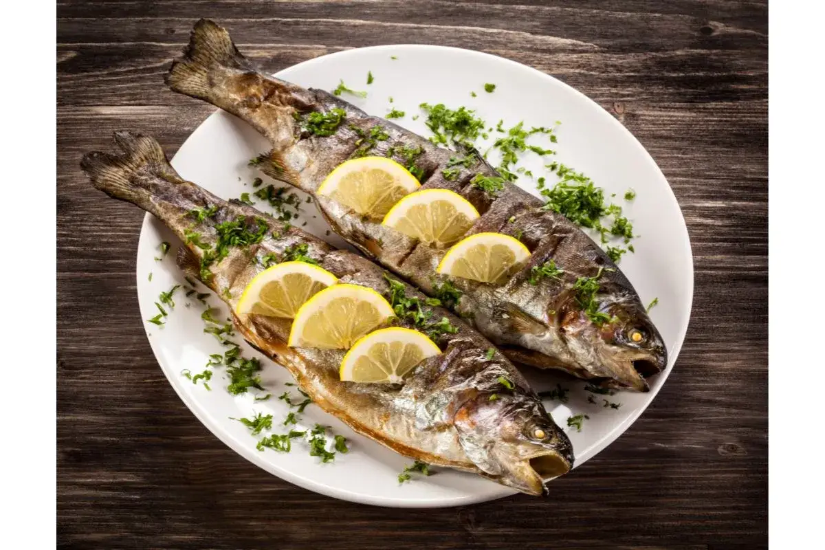 Deux truites entières grillées, garnies de rondelles de citron et de persil frais. Une parfaite recette truite barbecue pour un repas savoureux.