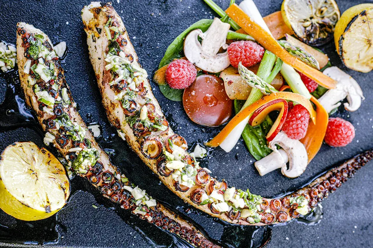 Tentacules de poulpe au barbecue, grill&eacute;s et garnis d'herbes fra&icirc;ches, servis avec des l&eacute;gumes croquants et des quartiers de citron grill&eacute;.