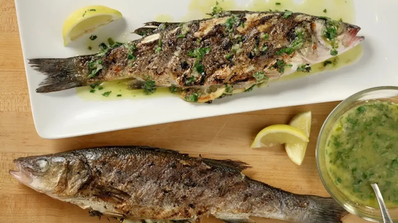 Deux poissons entiers grillés, assaisonnés d'herbes et de citron. Le temps de cuisson du poisson au barbecue est parfait pour cette présentation savoureuse.