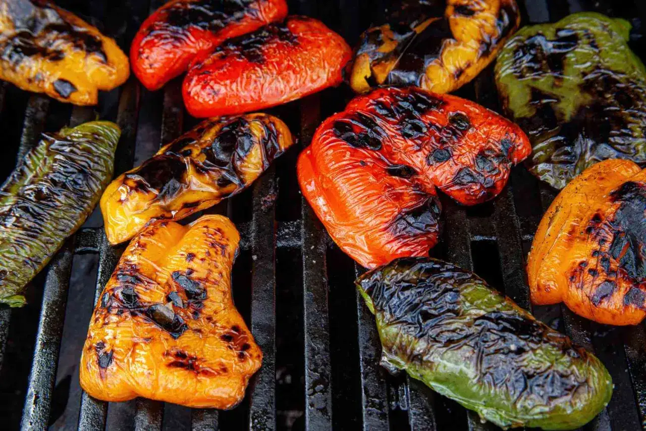 Poivrons rouges, jaunes et verts grillés sur un barbecue, leur peau noircie par les flammes, promettant une saveur fumée irrésistible.