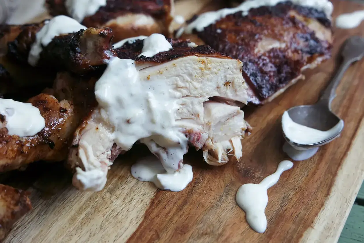 Poulet rôti juteux nappé d'une onctueuse sauce à l'ail, servi sur une planche en bois.