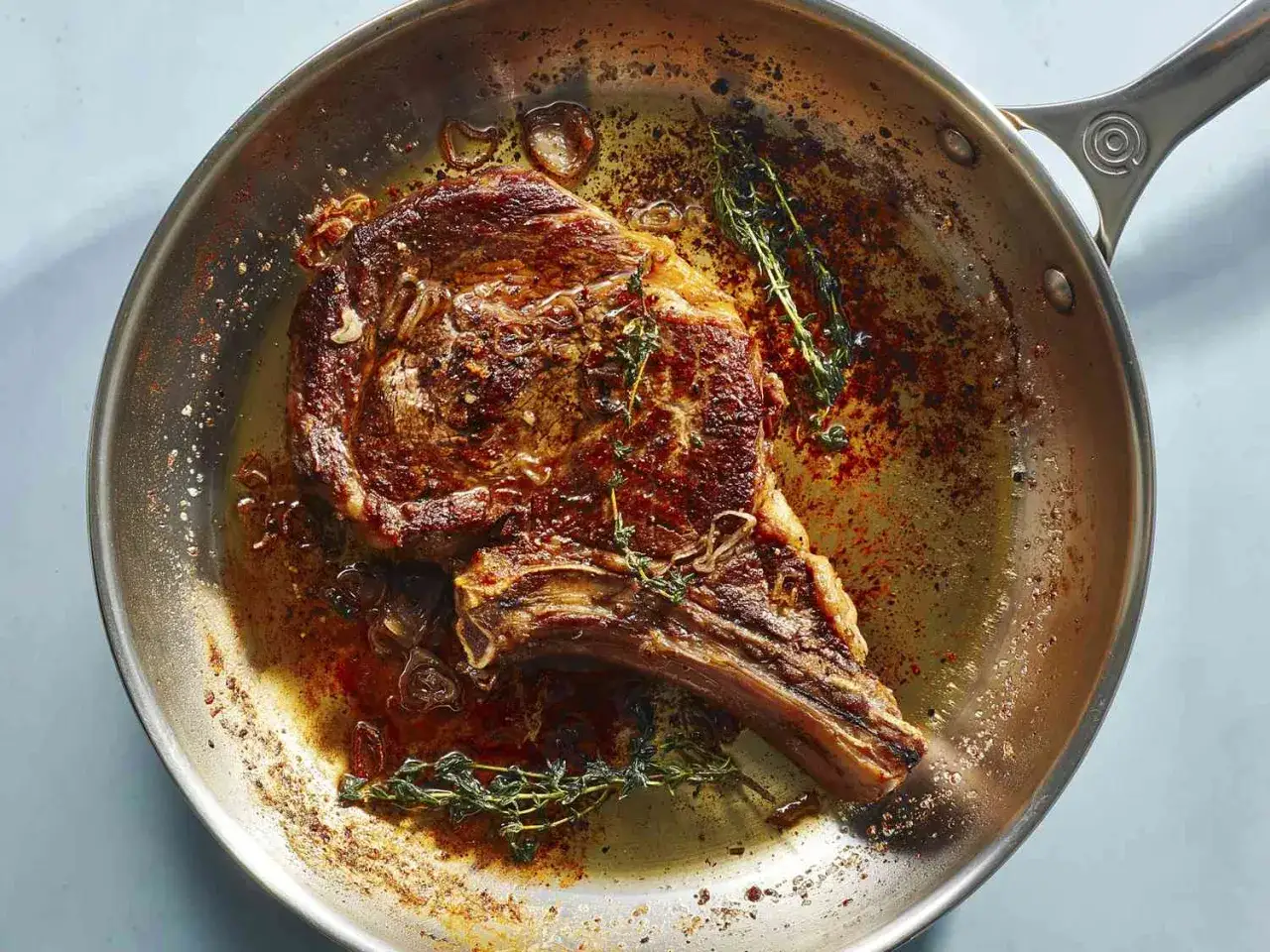 Une succulente entrecôte saignante cuit dans une poêle avec du thym et des oignons. La viande est dorée et juteuse.
