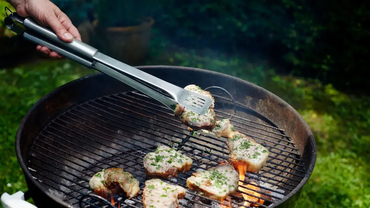 Viande assaisonnée sur un barbecue, le temps de cuisson barbecue avec couvercle approche. Des braises rougeoient sous la grille.