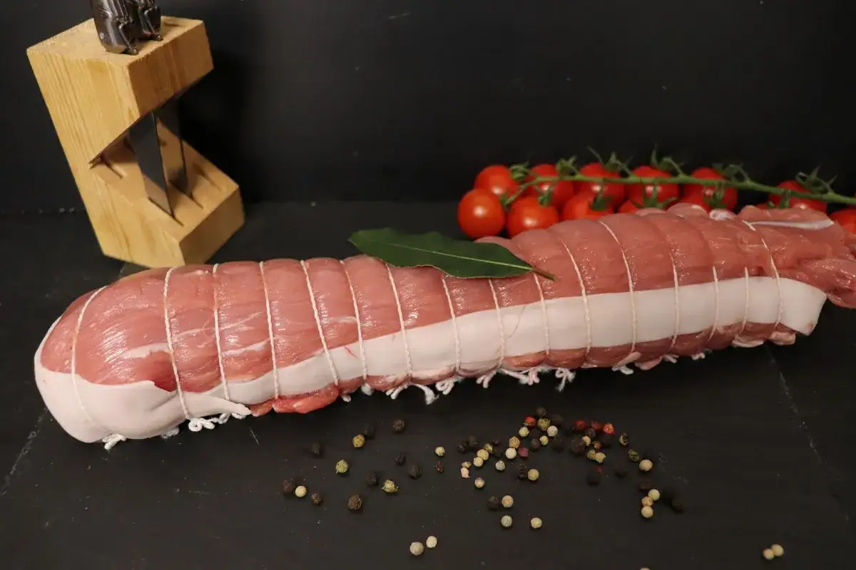 Filet mignon de veau ficelé, prêt à être cuisiné, avec des tomates cerises et des grains de poivre.