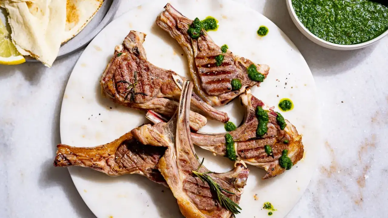 Côtelettes d'agneau grillées au barbecue, nappées d'une sauce verte vibrante. Un délice estival.