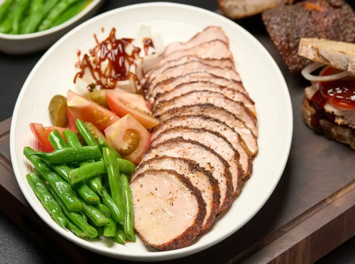 Tranches de longe de porc fumé, accompagnées de haricots verts, tomates, cornichons et sauce barbecue. Un délice à savourer !