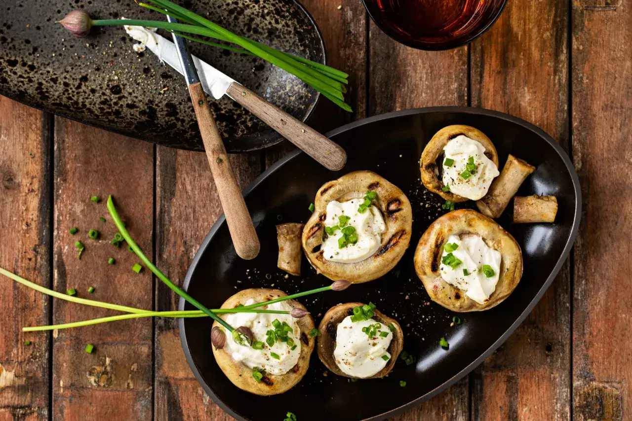 Champignons au barbecue farcis de fromage crémeux et garnis de ciboule fraîche. Un délice simple et savoureux.
