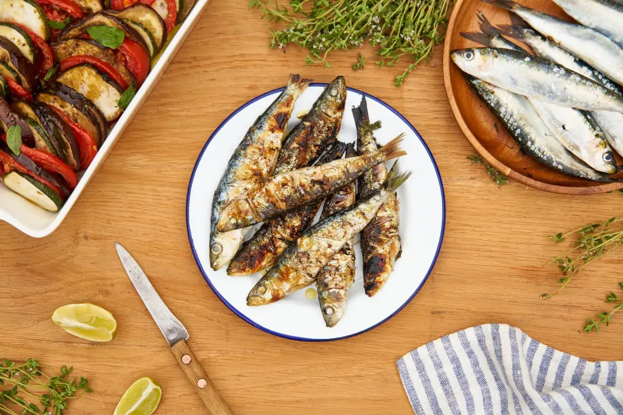 Poisson barbecue grillé sur une assiette blanche, accompagné de ratatouille, de citrons verts et de thym frais.