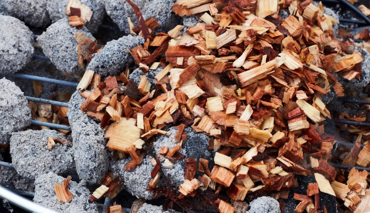 Charbons gris recouverts de copeaux de bois, pr&ecirc;ts pour comment allumer un fumoir et donner une saveur fum&eacute;e &agrave; vos grillades.