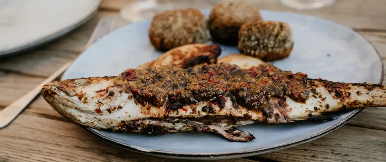 Un loup au barbecue, savamment garni d'une sauce aux herbes et tomates, accompagn&eacute; de petites boules de pain croustillantes.