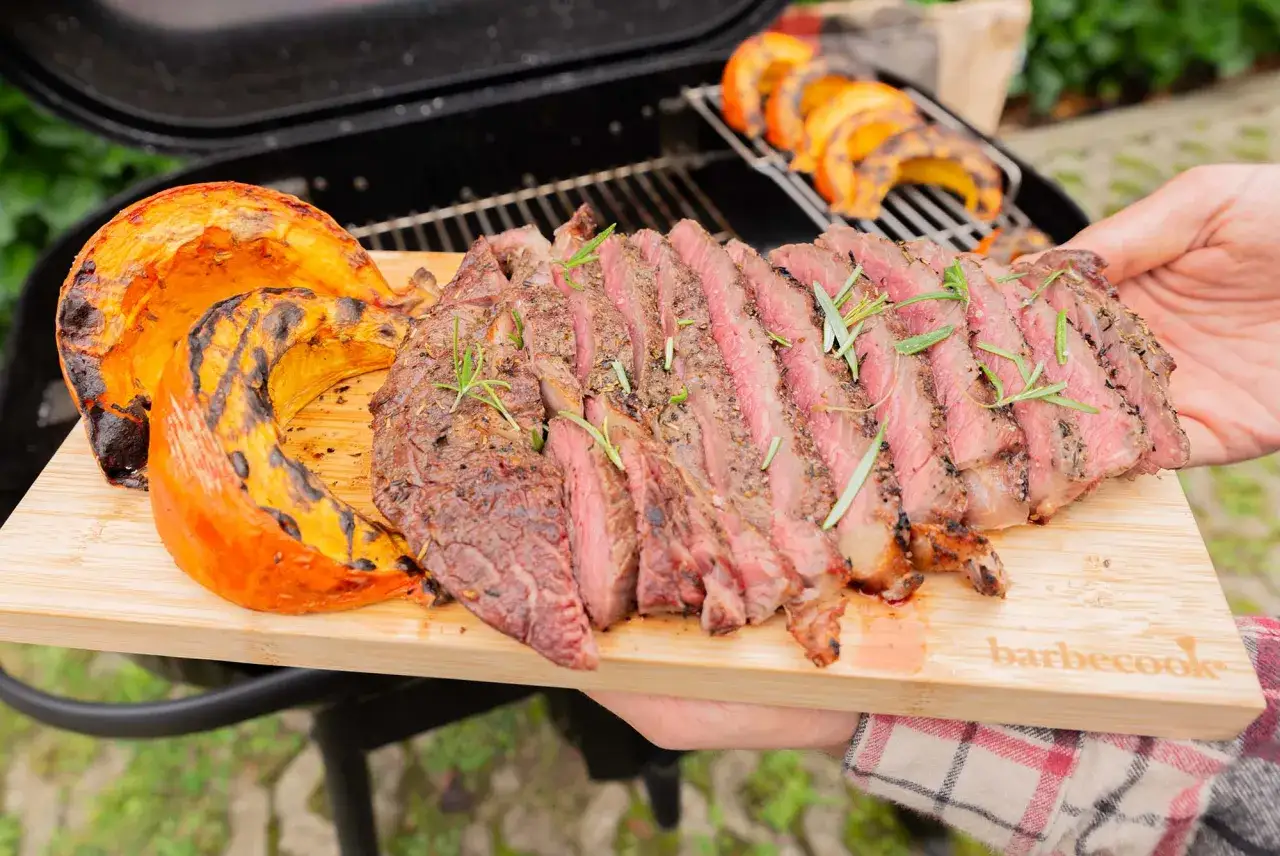 Un steak grill&eacute; et des quartiers de courge au barbecue, servis sur une planche en bois.