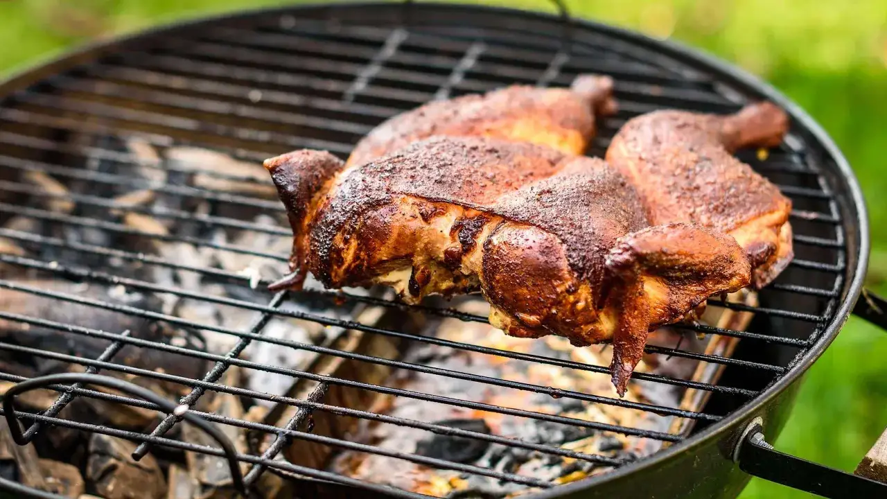 Morceaux de poulet au barbecue, dorés et juteux, cuisant sur un gril avec des braises ardentes en dessous.