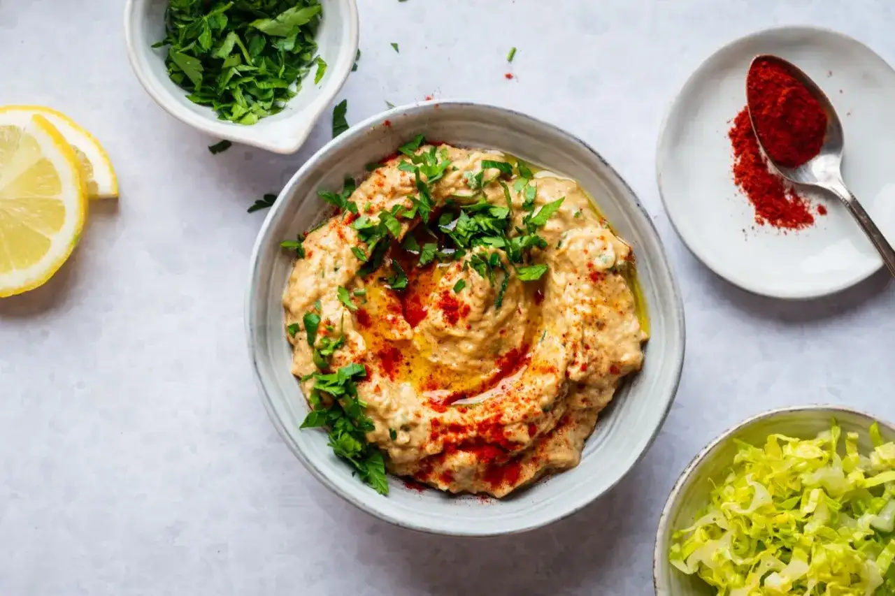 Un délicieux mutabal crémeux, garni de persil frais et de paprika, servi avec des quartiers de citron et de la laitue râpée.