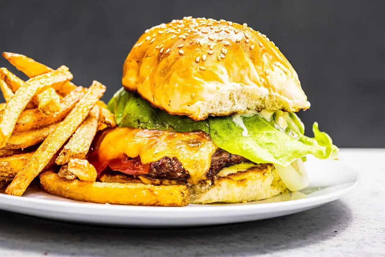 Un délicieux burger maison avec un pain aux sésames, de la laitue croquante, du fromage fondant et des frites dorées.