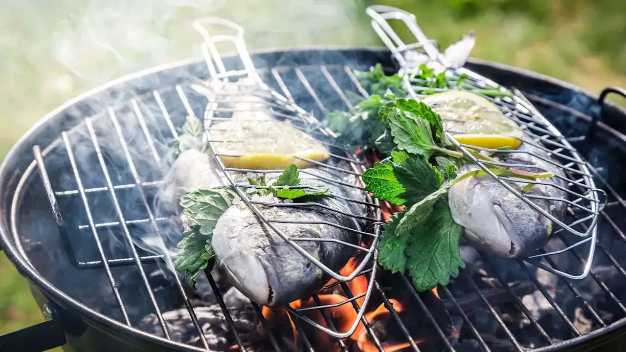 Filets de poisson au barbecue, fumants et aromatis&eacute;s au citron et aux herbes fra&icirc;ches, sur une grille au-dessus des braises ardentes.
