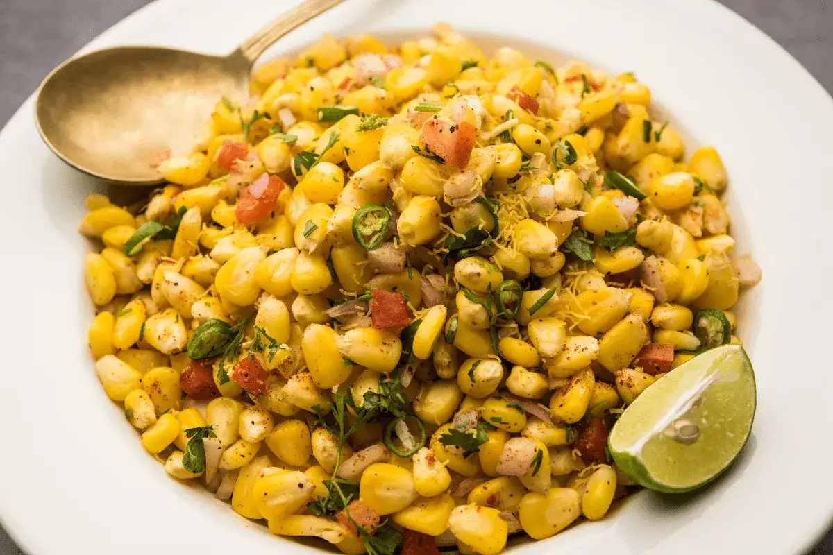 Salade de ma&iuml;s &eacute;pic&eacute;e, une recette facile avec des grains de ma&iuml;s, des tomates, des oignons, des piments verts et de la coriandre, garnie d'une tranche de citron vert.