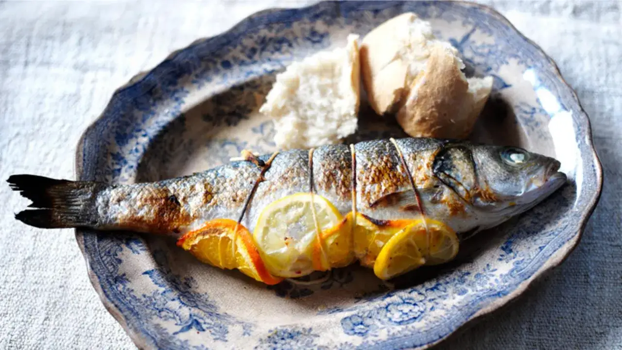 Poisson entier grillé avec des tranches de citron et d'orange, servi avec du pain sur une assiette décorée. Un délice de fenouil au barbecue.