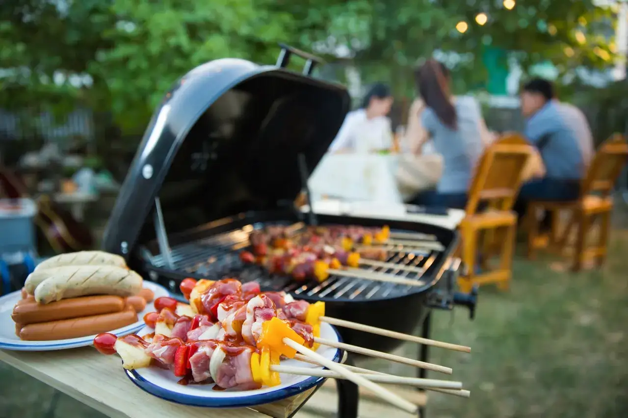 Brochettes et saucisses prêtes pour une soiree barbecue party. Des gens sont assis à une table en arrière-plan.