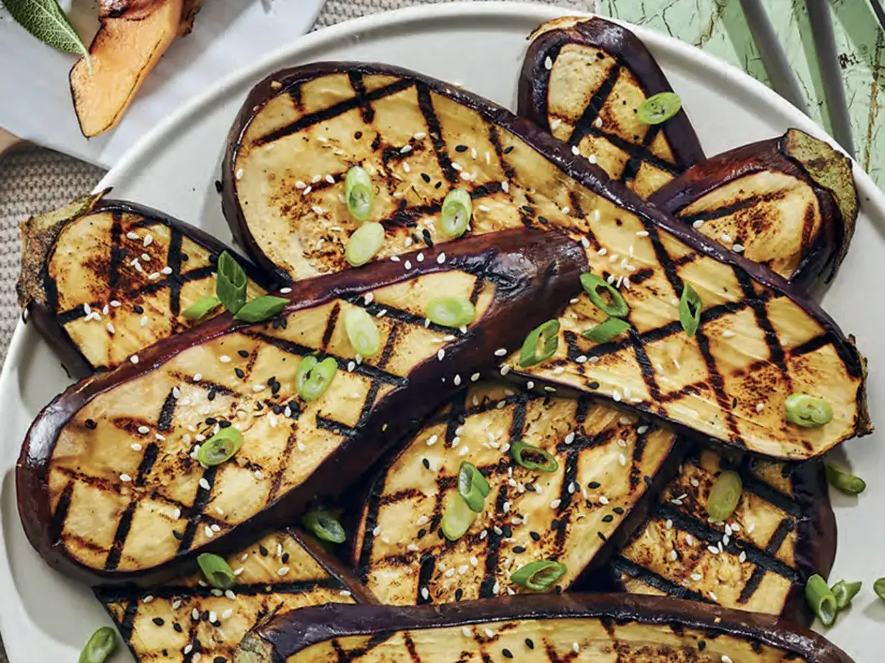 Tranches d'aubergine grillées au barbecue, parsemées de graines de sésame et de ciboule ciselée. Un délice estival !