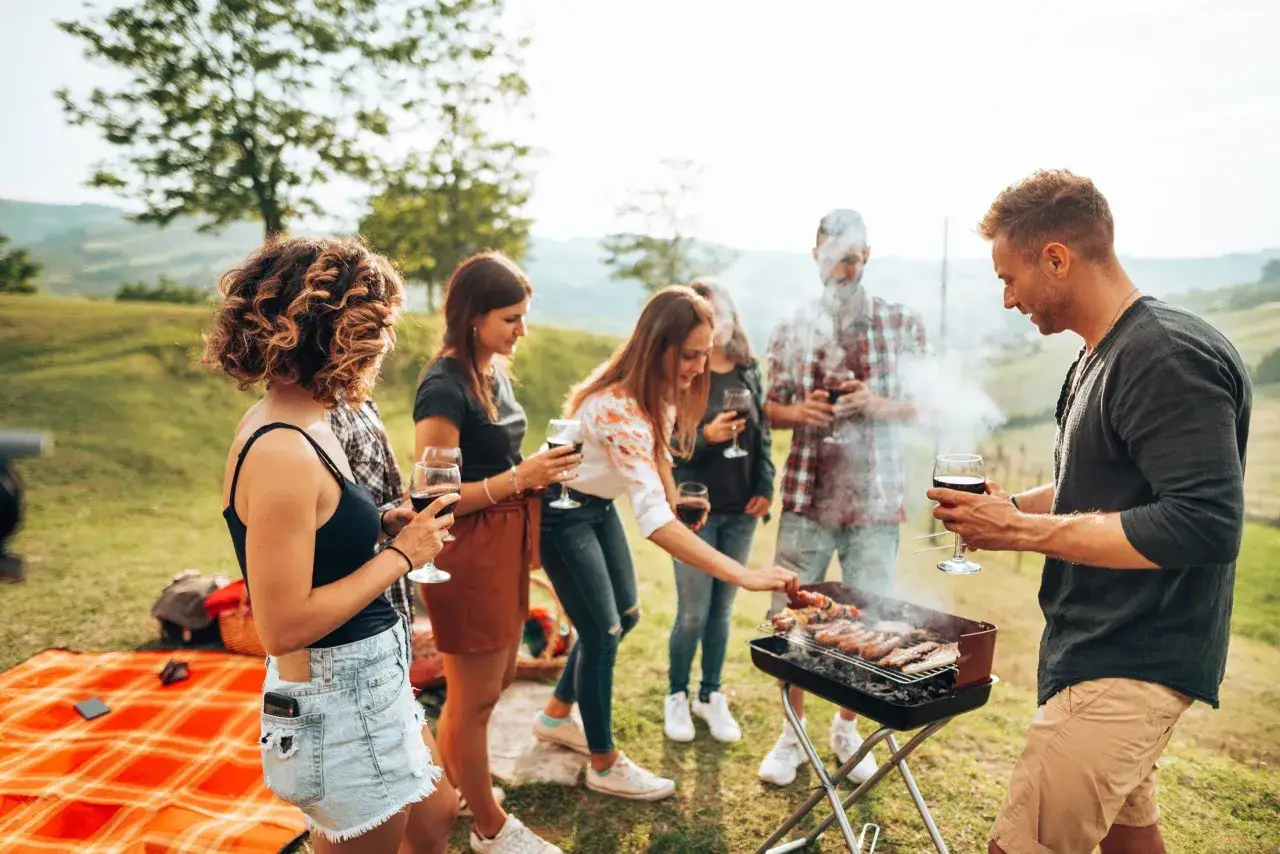 Un groupe d'amis profite d'un barbecue convivial en plein air, savourant des brochettes et du vin rouge dans un cadre champêtre.