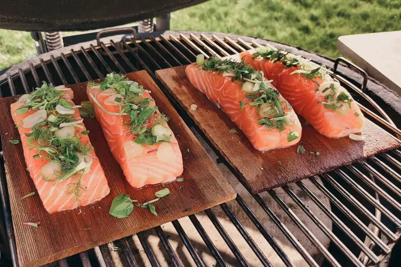 Quatre pavés de saumon sur planche de cèdre, garnis d'herbes fraîches et d'ail, prêts à griller.