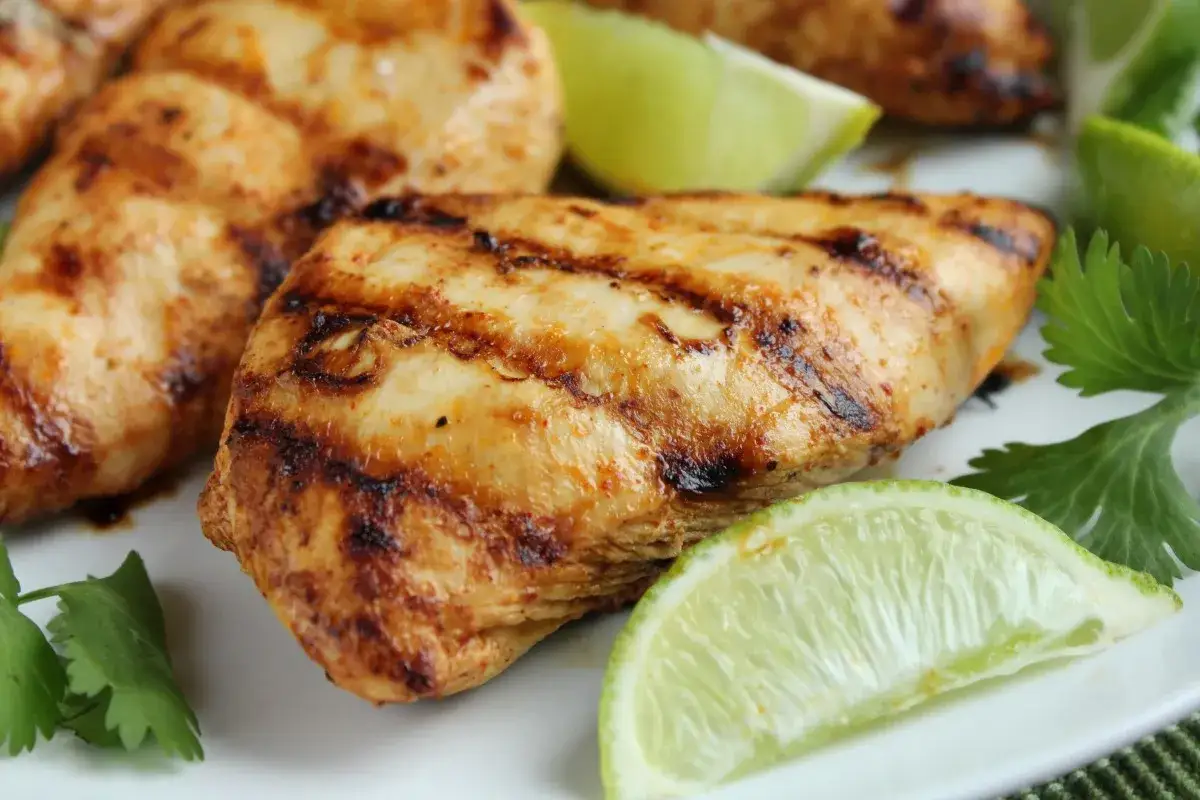 Poulet grillé aux marques de cuisson, parfumé d'une marinade mexicaine, garni de quartiers de lime et de coriandre fraîche.