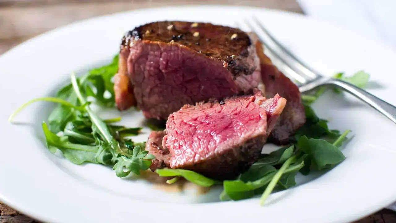 Un délicieux filet de bœuf saignant, servi sur un lit de roquette fraîche, prêt à être dégusté.