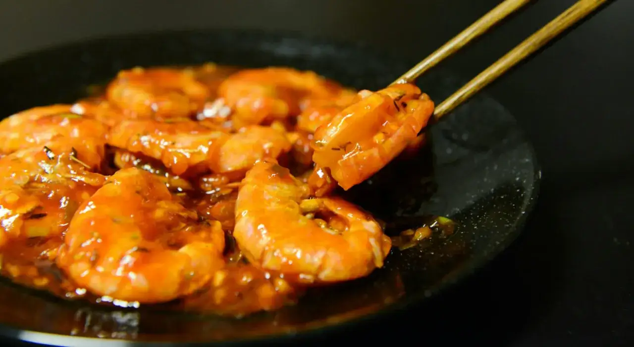 Crevettes sauce aigre-douce, une recette plancha facile et rapide. Une crevette est soulevée avec des baguettes.
