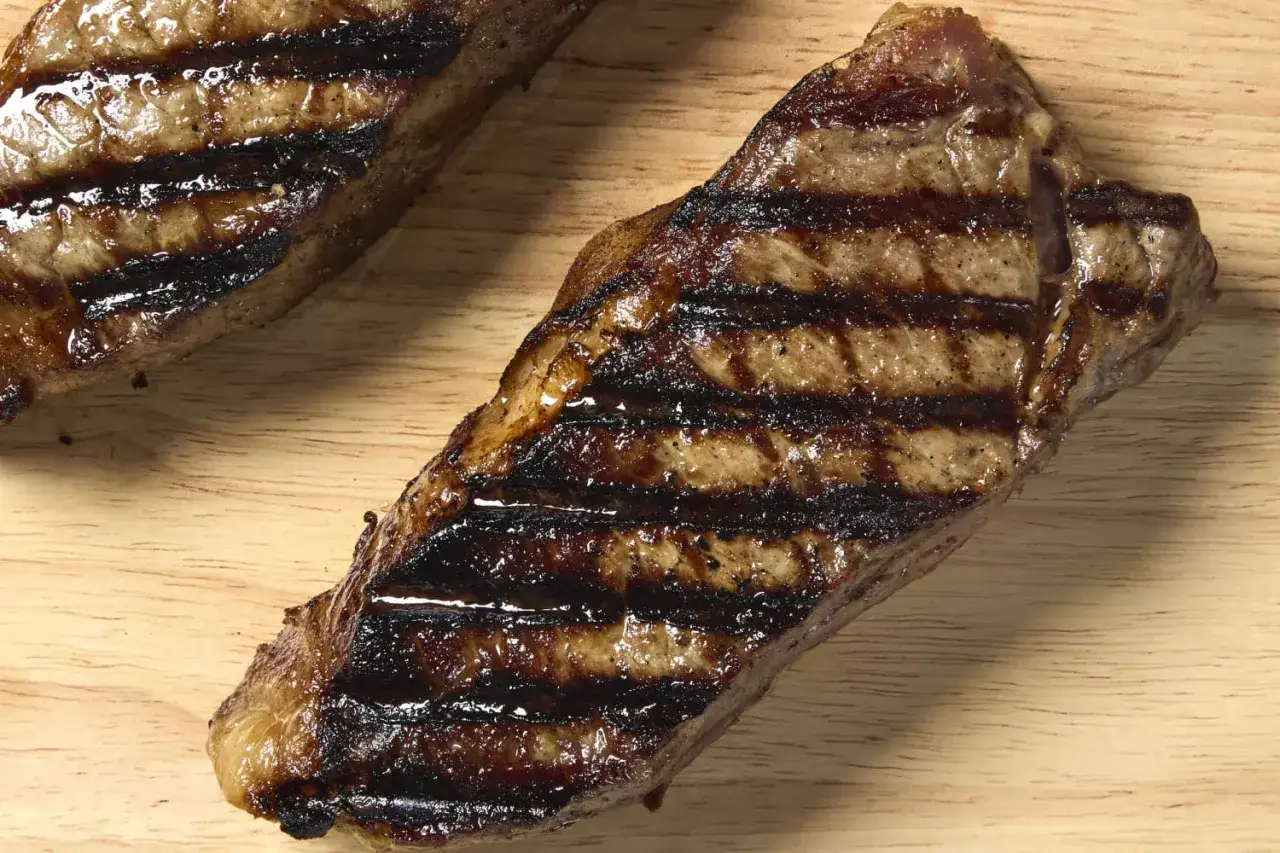 Deux entrecôtes grillées, savoureuses et juteuses, posées sur une planche en bois. Parfaites pour un repas gourmand.