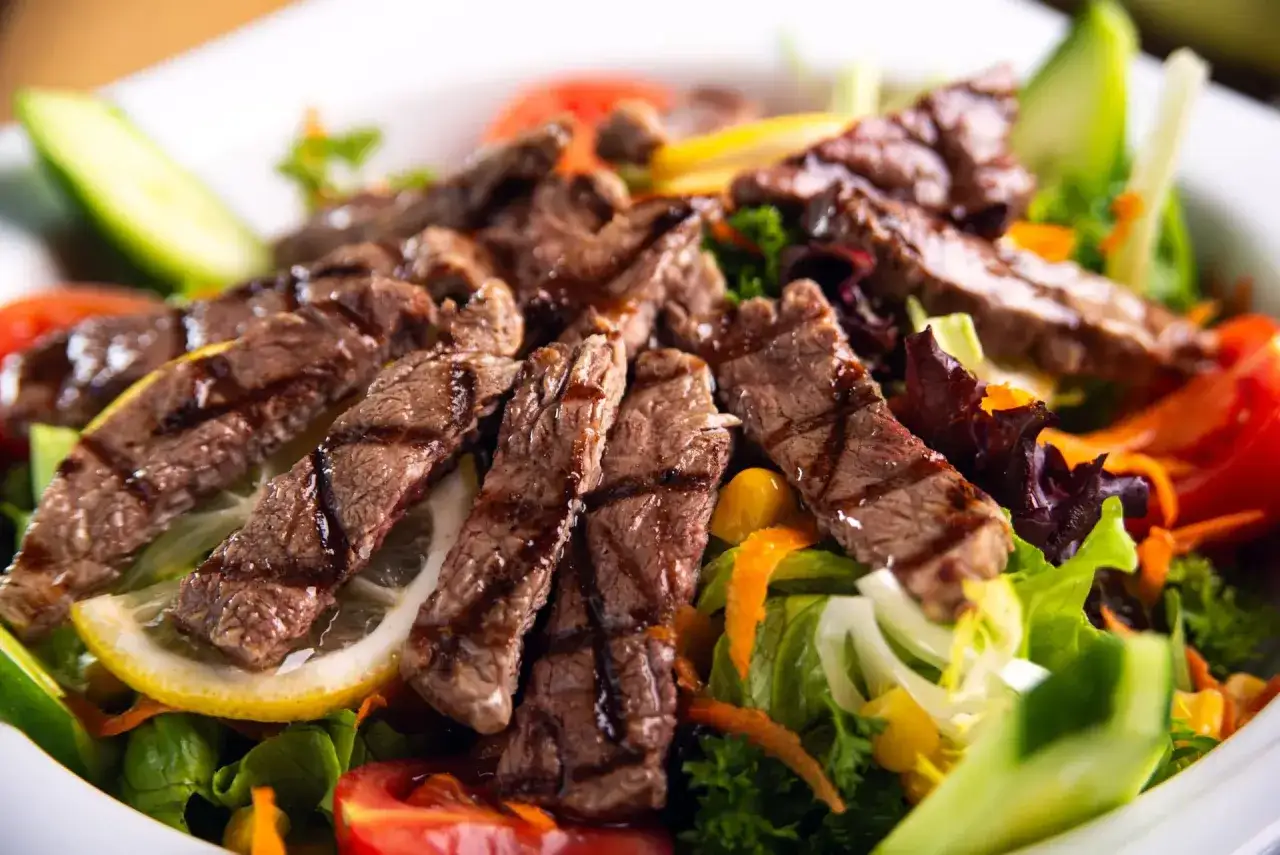 Salade de bœuf grillé avec légumes frais, arrosée d'une vinaigrette légère.