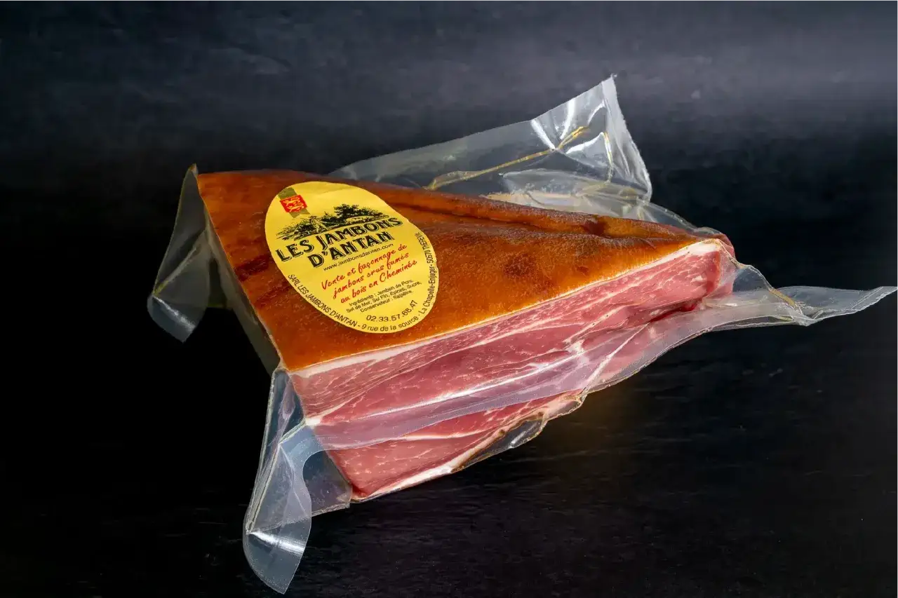 Un jambon fumé à froid, emballé sous vide, prêt à être dégusté. La belle couleur rosée de la viande contraste avec la croûte dorée.