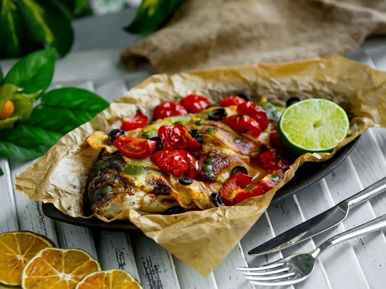 Dorade en papillote au barbecue, garnie de tomates cerises, olives et citron vert. Parfait pour un temps de cuisson savoureux.