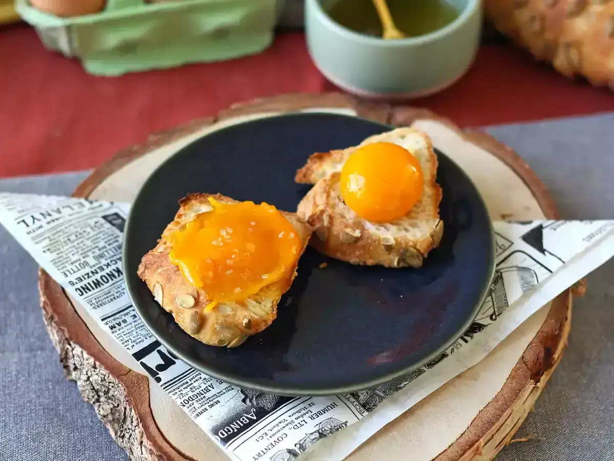Tranches de pain de campagne garnies d'une confiture orangée et d'un jaune d'œuf, prêtes à fumer le jaune.