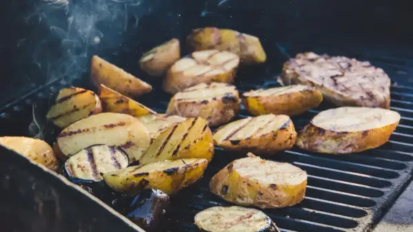 Pommes de terre coupées en quartiers, grillées à la perfection sur un barbecue, dégageant une fumée alléchante. Quelle pomme de terre barbecue !