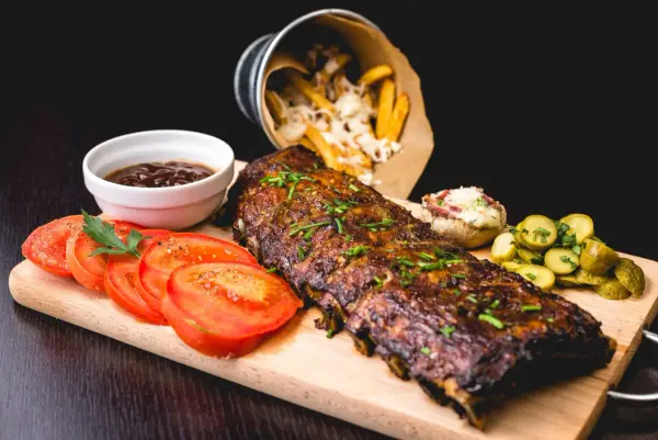 Délicieux ribs de porc, parfaitement cuits, accompagnés de frites, tomates et cornichons. Un festin pour les amateurs de cuisson ribs.