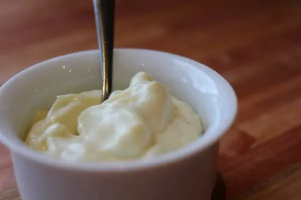 Une cuillère est plantée dans un bol de mayonnaise crémeuse, prête à être dégustée.