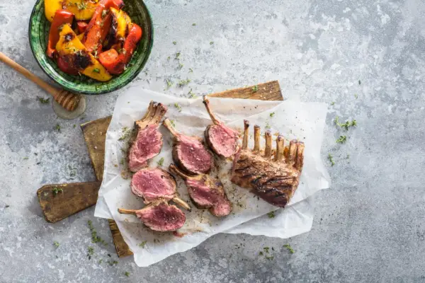 Un délicieux carré d'agneau au barbecue, coupé en côtelettes rosées, servi avec des poivrons grillés.